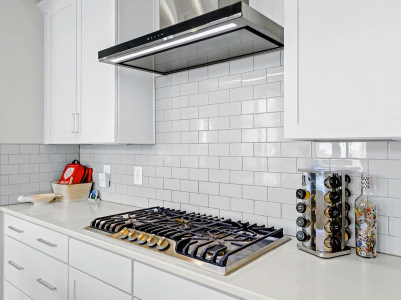 Kitchen - Five-burner gas cooktop close up under the steel hood, with subway tile and a spice tower right where you need them.
