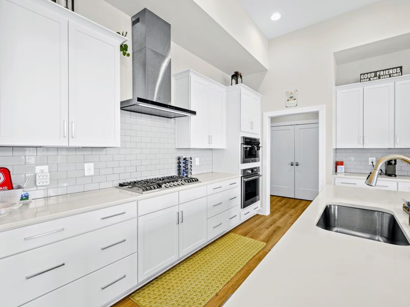 Kitchen - Gas cooktop and steel vent hood with subway tile backsplash, plus a deep undermount sink along the prep run.