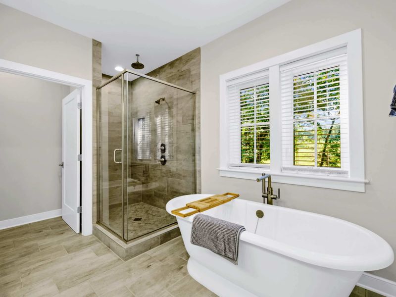 Primary Bath - Freestanding soaking tub beside the walk-in tile shower, bright windows and plantation blinds for soft light.