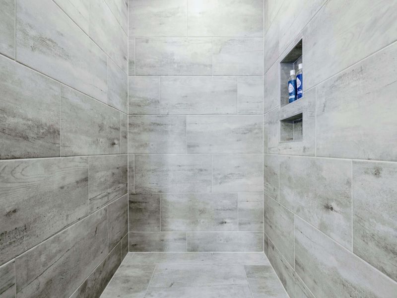 Primary Bath - Wide tile shower interior with stone-toned walls, a built-in niche, and herringbone floor tile underfoot.