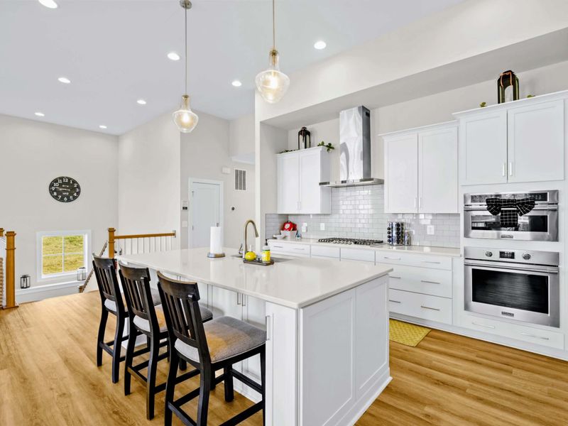 Kitchen - Three-stool island with cooktop, steel hood, and double ovens visible along the prep wall, all in one tidy zone.