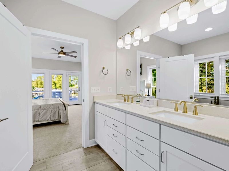 Primary Bath - Double vanity in brushed gold, the ensuite doorway opening straight to the primary bedroom and deck.