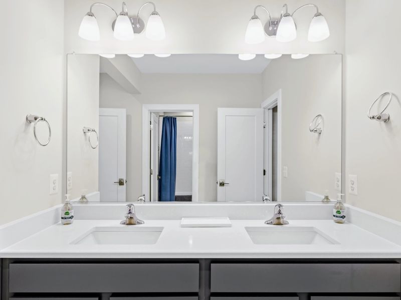 Suite 4 Bath - Wide double vanity with twin sinks and a bright mirror, dual entry doors at either side.