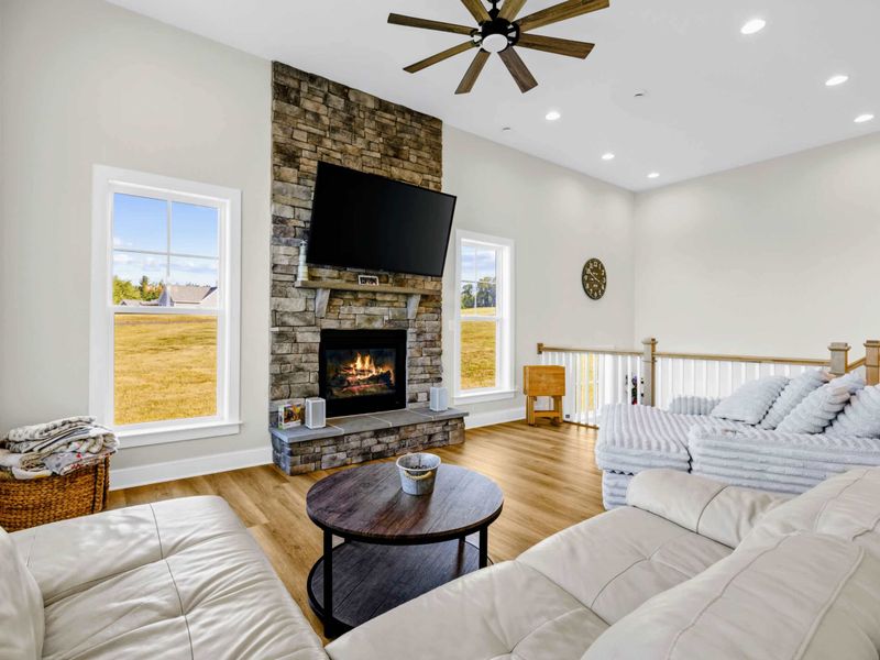 Great Room - Floor-to-ceiling stone fireplace under the big-blade fan, the heart of the open layout where everyone lands.
