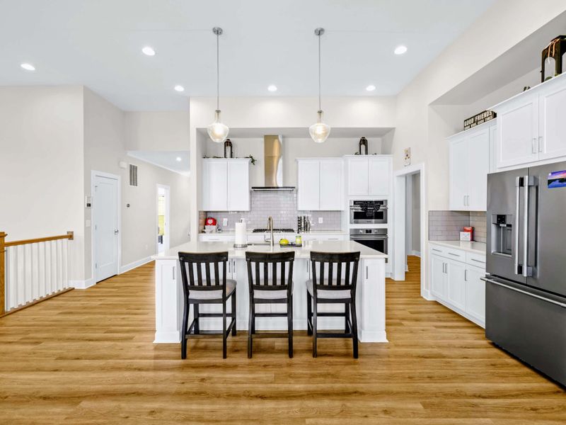 Kitchen - Bright, open, and ready for a cook: wide quartz island, gas range under the steel hood, and a full row of stools.