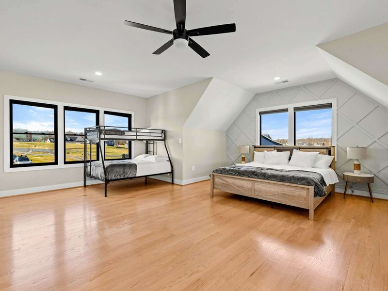 Suite #5: Spacious bedroom with a king-sized bed and a twin-over-full bunk bed. Features hardwood floors, a coffered accent wall, and large windows with scenic views.