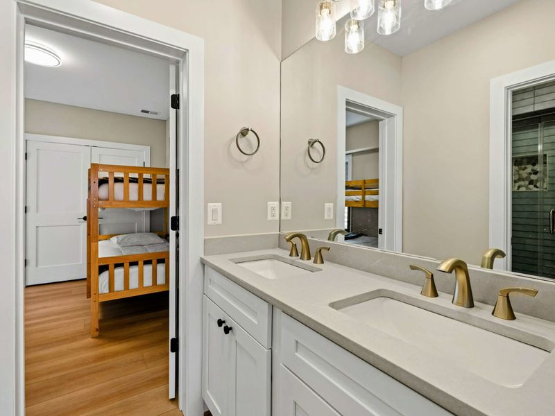 Jack & Jill Bathroom: Shared between Suite #7 and Suite #8, featuring dual sinks with brushed gold fixtures, a spacious vanity, and a glass-enclosed walk-in shower with elegant tile accents.