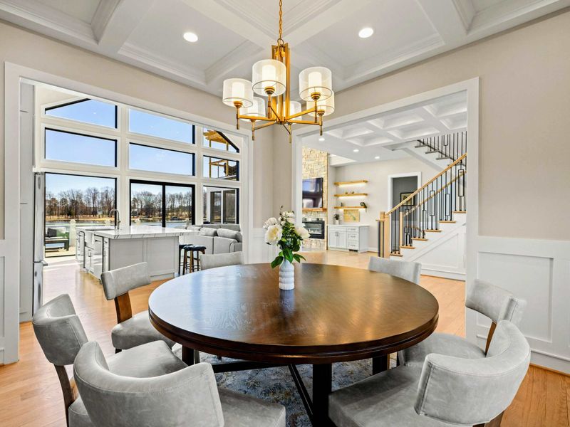 Sophisticated Dining Room: Beautifully designed space with a coffered ceiling, elegant chandelier, and an open layout that flows seamlessly into the great room, offering stunning lake views for a refined dining experience.