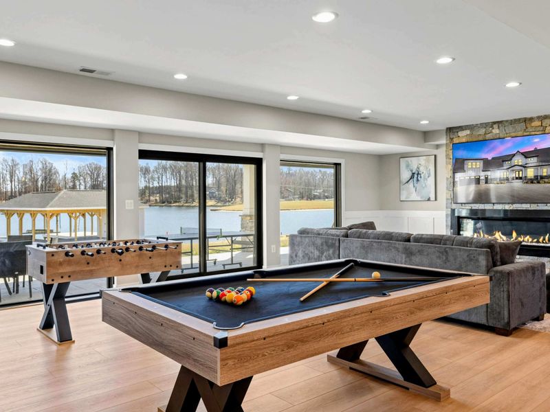 Game Room: Spacious entertainment area featuring a pool table, foosball, comfortable seating, cozy fireplace, and panoramic lake views, perfect for family fun and friendly competition.