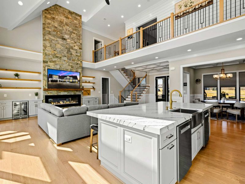 Open-Concept Elegance: This breathtaking space seamlessly blends the gourmet kitchen, great room, and dining area, featuring soaring ceilings, a grand stone fireplace, and a stylish mezzanine overlooking the living area.