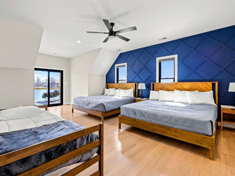 Suite #4: Spacious and stylish bedroom featuring two king beds, a twin bed, a bold navy accent wall, and private balcony access with stunning lake views—perfect for a comfortable retreat.