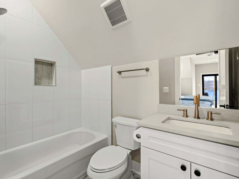 Suite #4 En-Suite Bathroom: Features a bathtub/shower combo, white vanity with quartz countertop, and brushed gold fixtures. A built-in shower niche offers convenient storage.