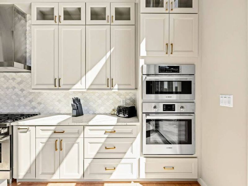 Premium Kitchen Appliances: A sleek and modern kitchen equipped with built-in stainless steel double ovens, custom cabinetry, and a stylish backsplash, combining elegance with top-tier functionality.