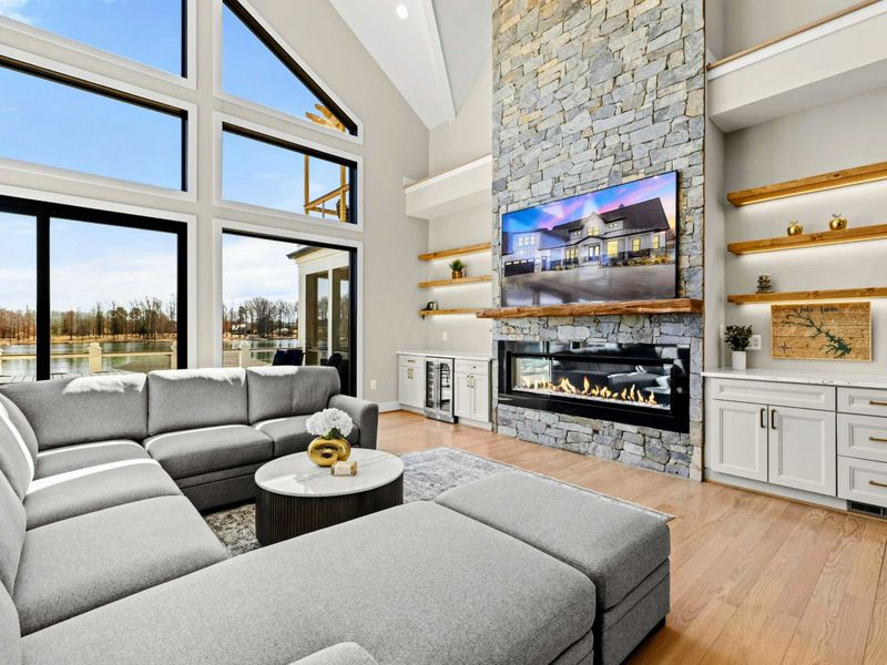 Great Room: Breathtaking open-concept space with soaring ceilings, a grand stone fireplace, floor-to-ceiling windows showcasing stunning lake views, and a spacious sectional for ultimate relaxation.