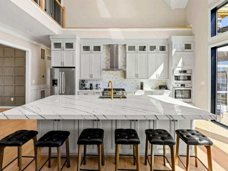 Gourmet Kitchen: Elegant and spacious kitchen featuring a massive quartz island with seating for six, custom cabinetry, high-end appliances, and a stylish backsplash, perfect for cooking and gathering.