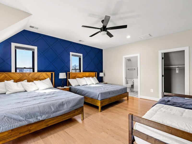 Suite #4: A spacious bedroom with **two king-sized beds** and a twin bed. The bold navy accent wall adds sophistication, complemented by modern lighting and a ceiling fan. Includes a private en-suite bathroom and walk-in closet for comfort and conven