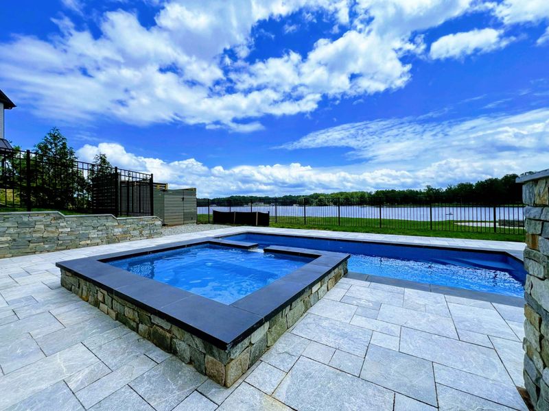 Spa - Raised stone spa with lake views beyond the iron fence, connected to the main pool by a water spillover.