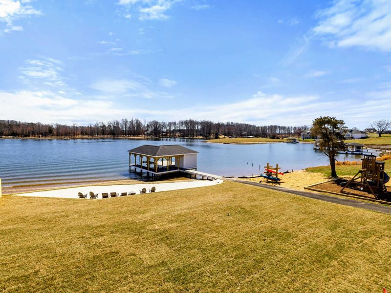Expansive Backyard: Beautifully manicured lawn gently slopes down to a private sandy beach, dock, and play area, all framed by stunning panoramic views of Lake Anna.