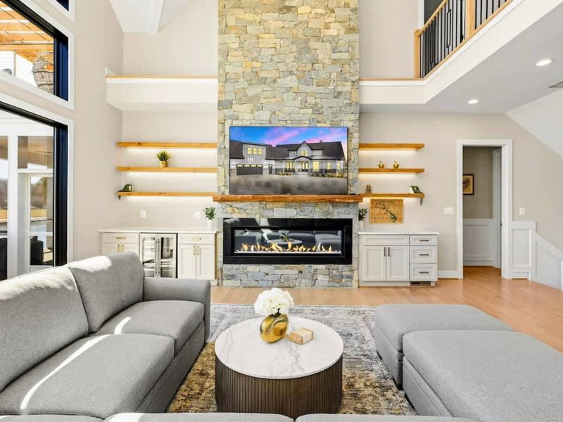 Great Room: Elegant and inviting space featuring a towering stone fireplace, custom built-ins, a plush sectional, and stunning natural light from expansive windows overlooking Lake Anna.