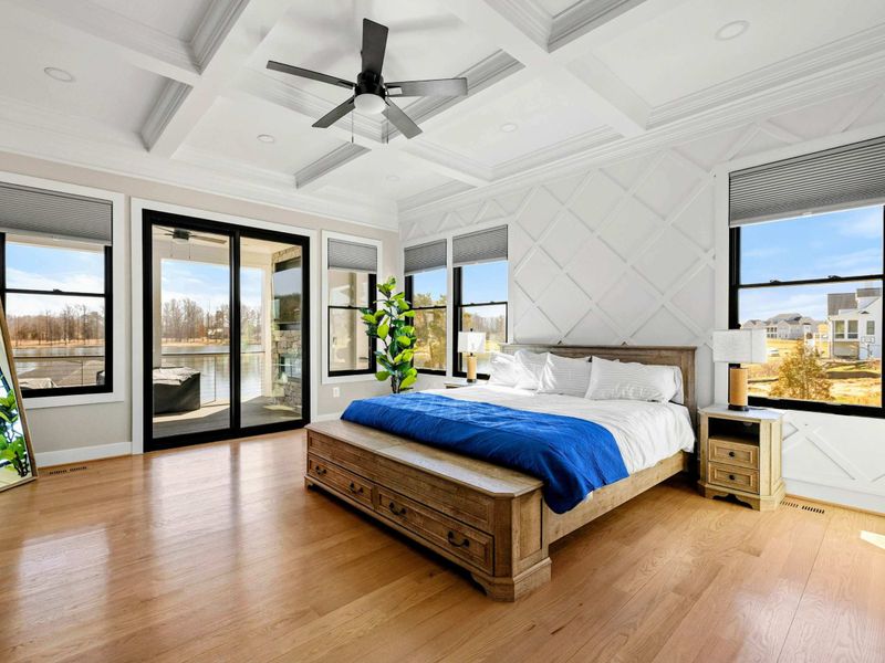 Primary Suite: Elegant and serene retreat featuring a coffered ceiling, luxurious king bed, private patio access, and expansive windows showcasing breathtaking lake views.