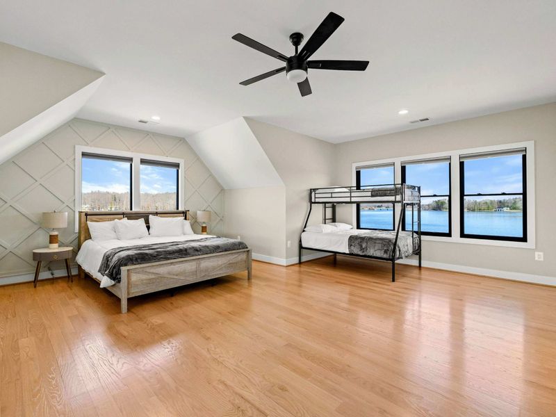 Suite #5: Spacious bedroom featuring a king-sized bed and a twin-over-full bunk bed. Offers hardwood floors, a coffered accent wall, and large windows with scenic lake views.