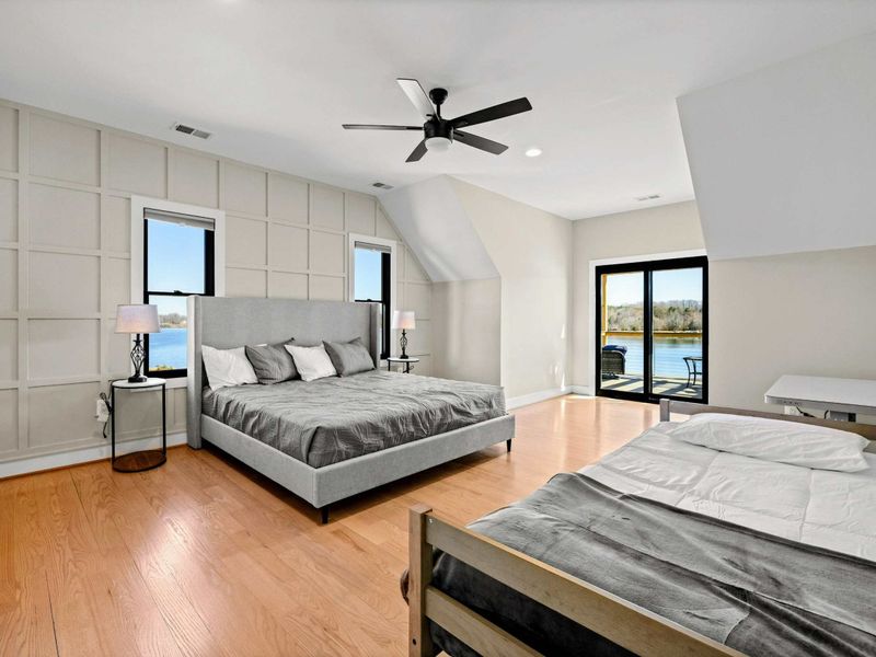 Suite #3: Elegant and spacious bedroom featuring a king bed, an additional twin bed, a stylish accent wall, private balcony access, and breathtaking lake views for a serene getaway.