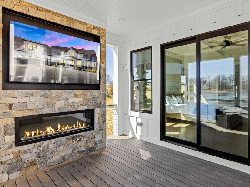 Cozy Outdoor Fireplace: Inviting covered deck space featuring a modern stone fireplace, mounted TV, and seamless access to the primary suite—perfect for enjoying crisp evenings with warmth and entertainment.
