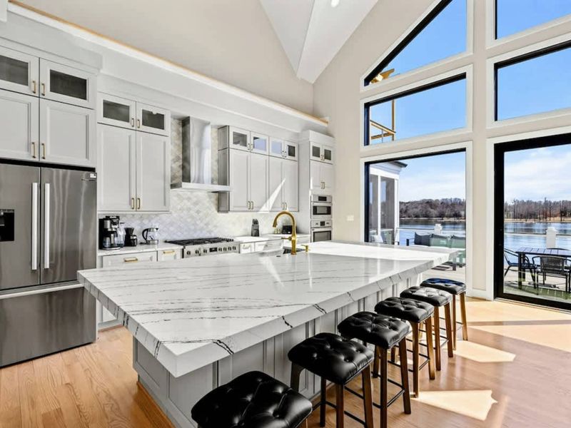 Gourmet Kitchen: Stunning chef’s kitchen featuring sleek quartz countertops, high-end stainless steel appliances, a spacious island with seating, and breathtaking lake views through soaring windows.