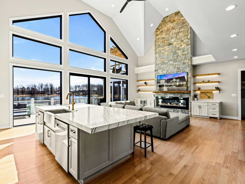 Open-Concept Living: Stunning fusion of the gourmet kitchen and great room, featuring soaring ceilings, a grand stone fireplace, floor-to-ceiling windows, and breathtaking lake views for a seamless and luxurious living experience.