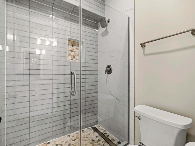 Jack & Jill Bathroom: Features a glass-enclosed walk-in shower with stylish tilework, a built-in niche, and a pebble stone floor, creating a modern and refreshing space.
