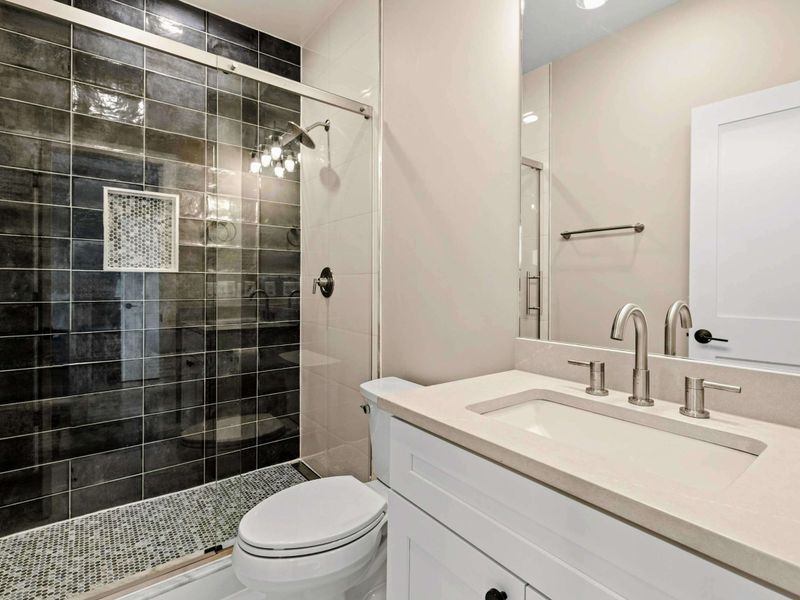 Suite #6 Bathroom: Sleek design with a spacious walk-in shower, bold black tile, glass door, and built-in niche. The vanity features an undermount sink with brushed nickel fixtures for a modern touch.