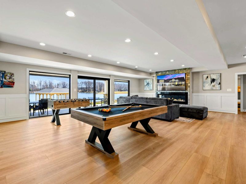 Game Room: Spacious entertainment hub featuring a sleek pool table, foosball, a cozy sectional by the fireplace, and stunning lake views, creating the perfect spot for fun and relaxation.