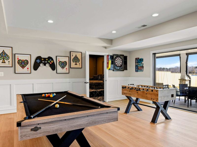 Ultimate Game Room: A lively entertainment space featuring a pool table, foosball, dartboard, and stylish gaming-themed decor, with easy access to the outdoor patio and scenic lake views.