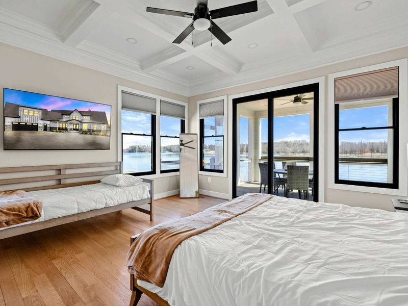Suite #2: Stunning lakefront bedroom featuring a king bed, additional twin bed, coffered ceiling, a mounted TV, and private patio access with breathtaking waterfront views.