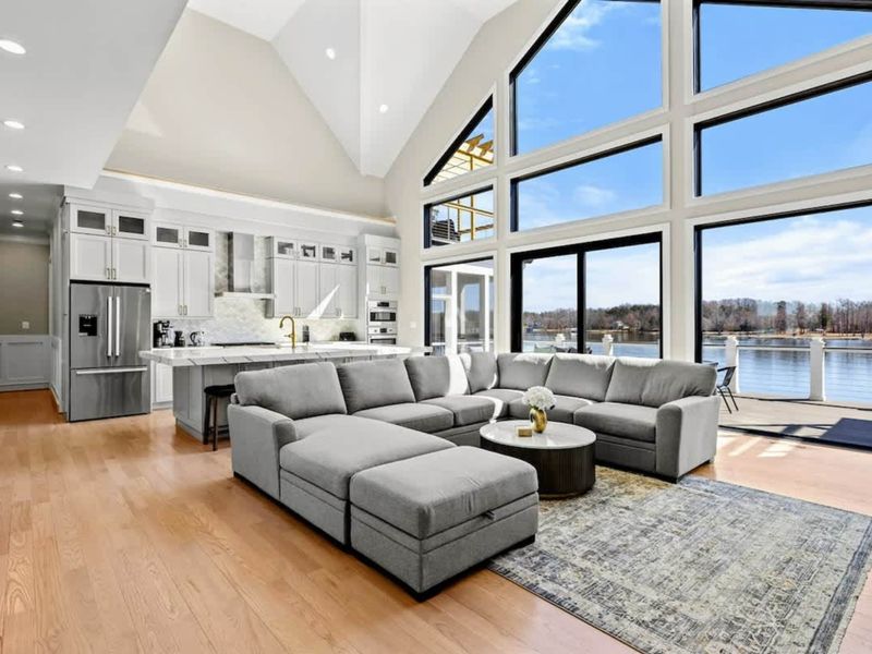 Great Room: Expansive, light-filled space featuring floor-to-ceiling windows with breathtaking lake views, a plush sectional for ultimate comfort, and a seamless open layout connecting to the gourmet kitchen.