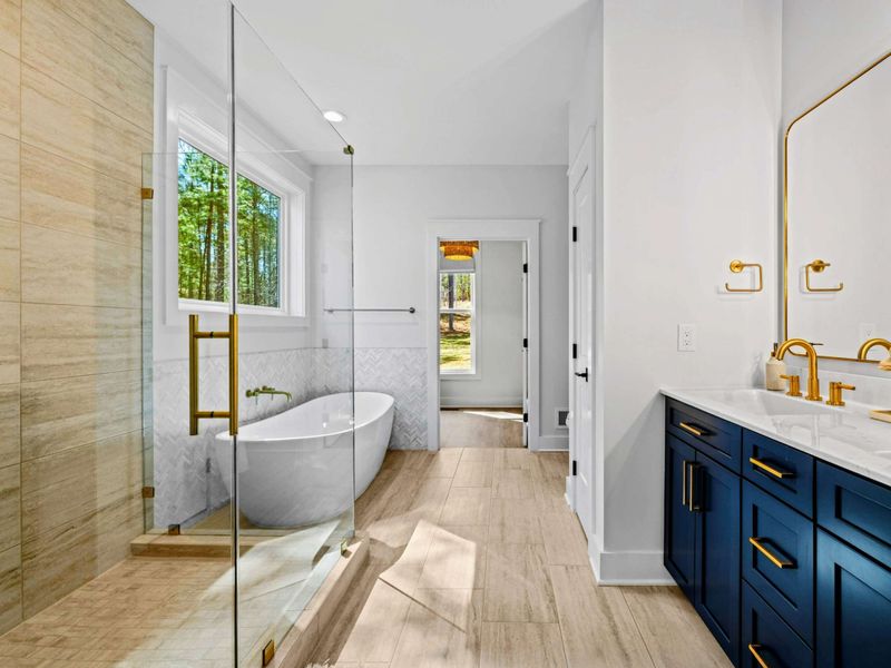 Primary Bath - A freestanding soaking tub sits beneath a window of woods, with a tiled walk-in shower and double vanity completing the retreat.
