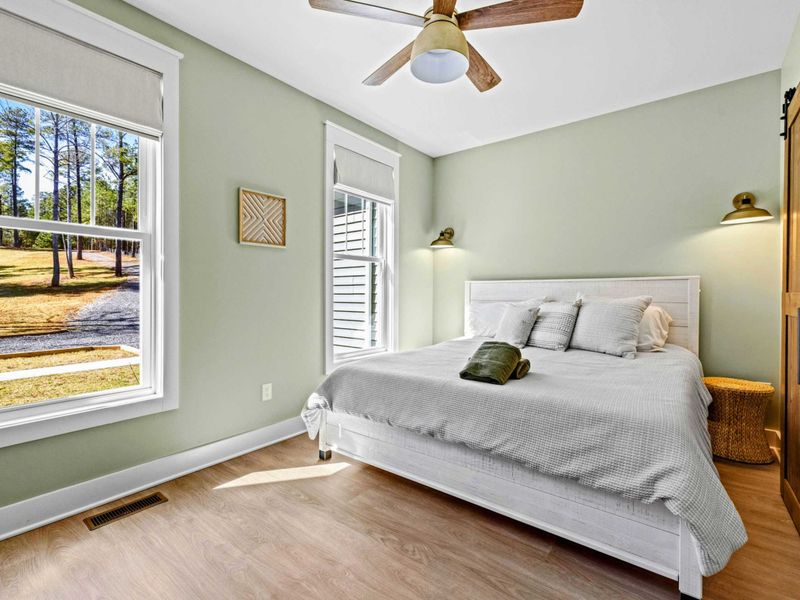King Ensuite - A second main-level suite in soft green, with a king bed, barn-door bath, and woods views for easy privacy.