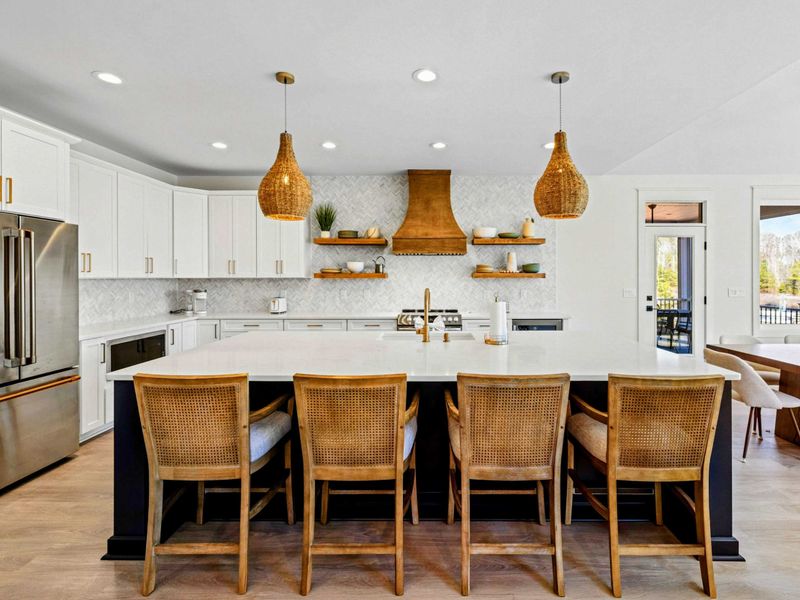 Chef's Kitchen - A massive quartz island seats four beneath woven pendants, with a statement wood hood and stainless appliances open to the dining and lake views.