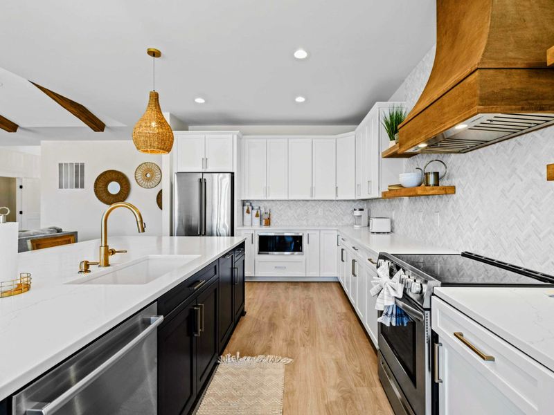 Kitchen - The navy island and brushed-gold fixtures pop against white cabinetry and a marble herringbone wall, open to the living room and lake.