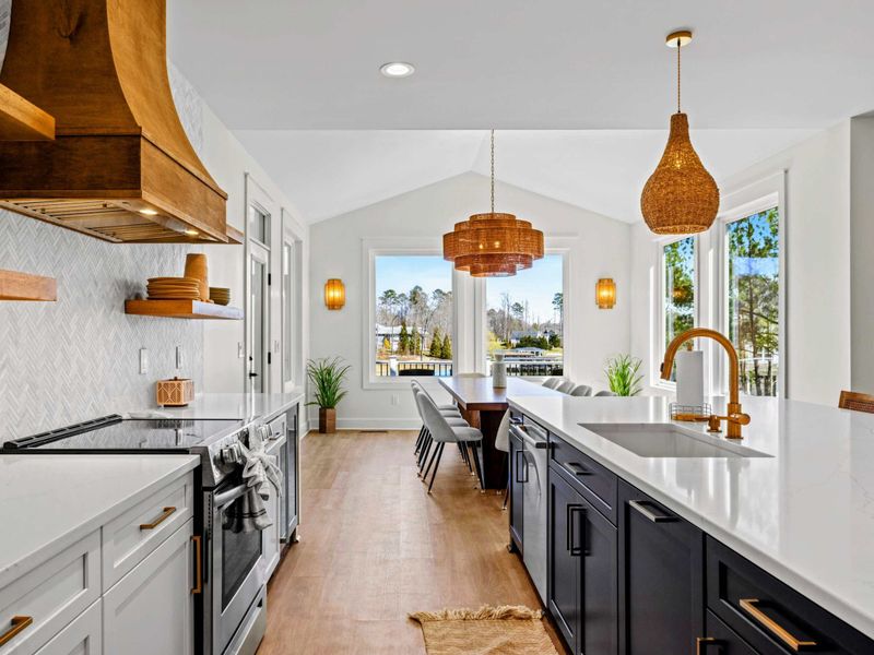 Kitchen & Dining - The island anchors a galley of stainless appliances and gold fixtures, with the long dining table and lake views just steps away.