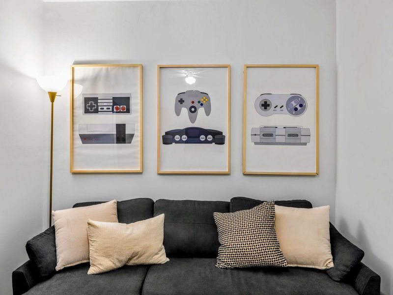 Retro Vibes – Nostalgic wall art celebrates classic game consoles, adding playful personality to this lounge-worthy corner with cushy seating and a cozy atmosphere.