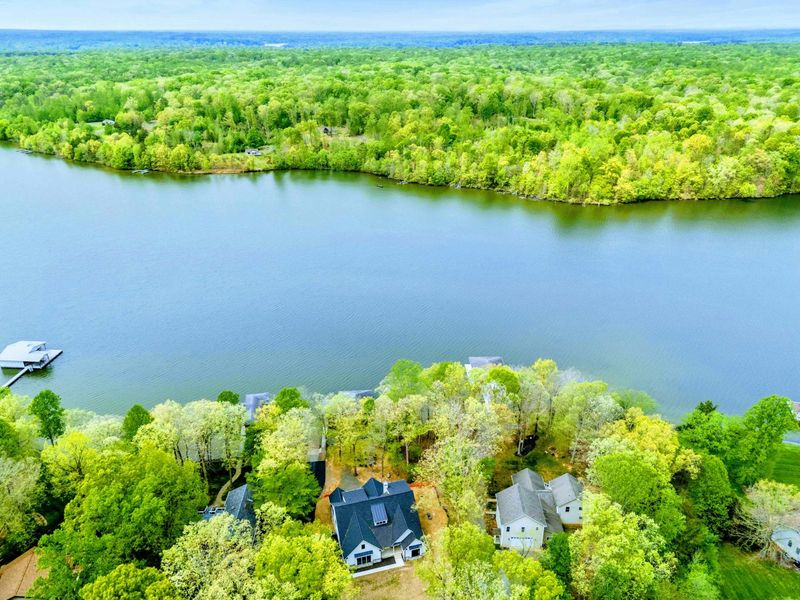 Aerial - Overhead view of the property nestled among mature trees on the waterfront with the covered dock and boathouse below.