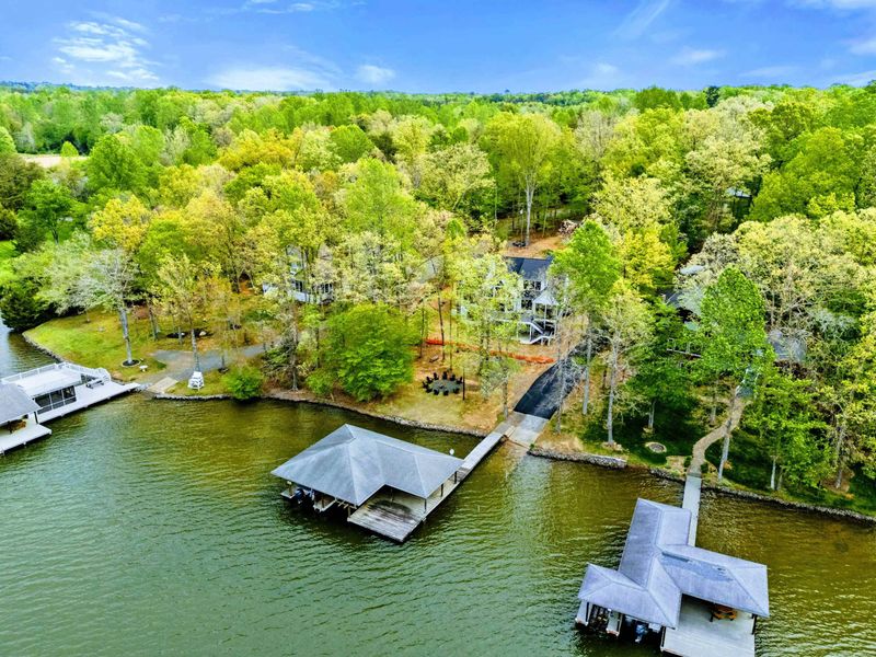 Aerial - Broader view of the wooded waterfront lot, dock, and surrounding cove from above.
