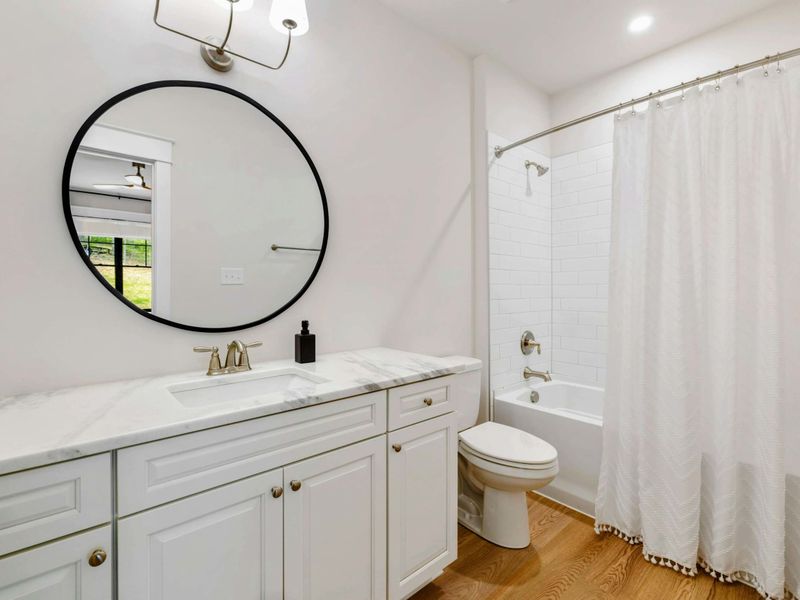 Bathroom - White vanity with marble top, round black-framed mirror, and a tub/shower combo with subway tile.