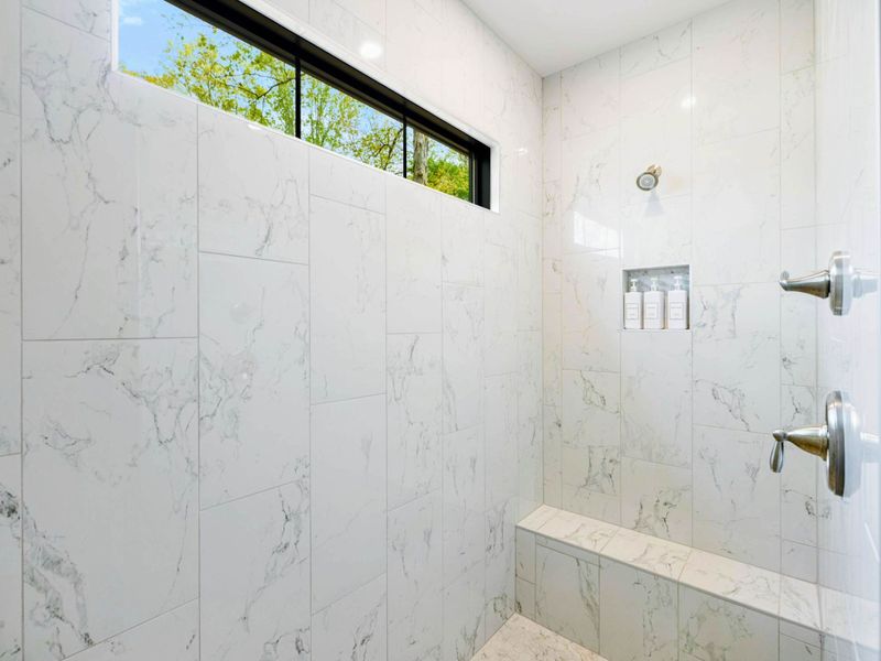Primary Bathroom - Walk-in shower with marble-look tile, a built-in bench, and a clerestory window for natural light.