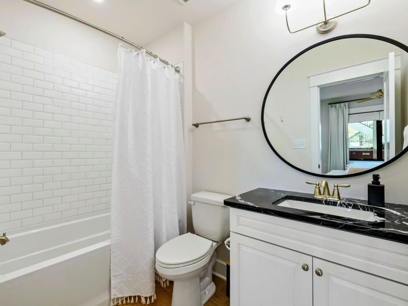 Bathroom - Tub and shower combo with white subway tile, black marble vanity top, and gold fixtures.