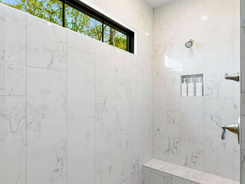 Primary Bathroom - Rain showerhead and marble tile with a bench seat beneath the clerestory window.
