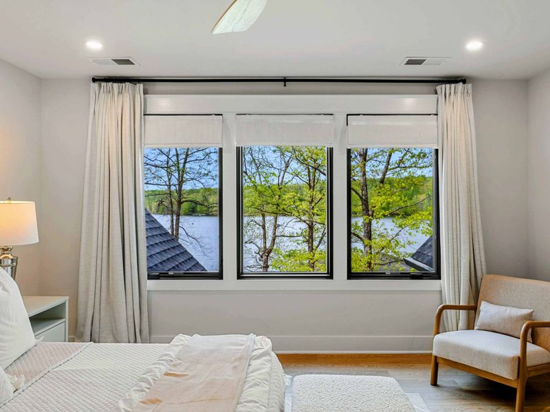 Primary Suite - Wide windows frame views of the lake and trees, with an accent chair for relaxing in the morning light.