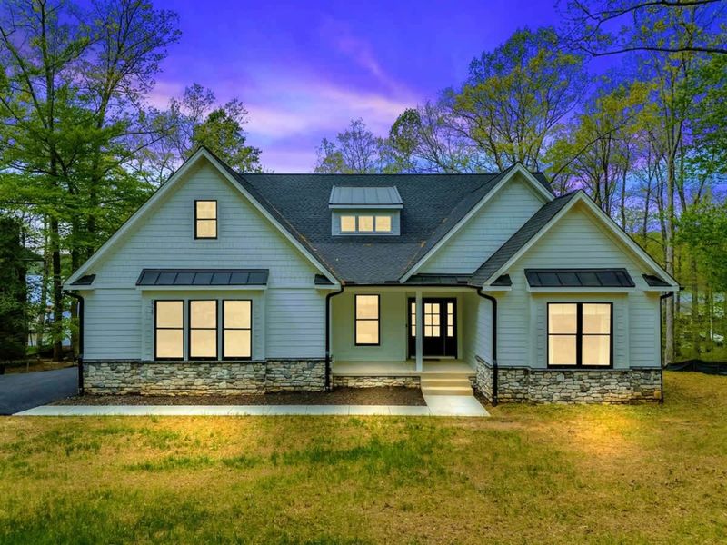 Exterior - Modern farmhouse with gray siding, stone accents, a covered front porch, and gabled dormers at dusk.