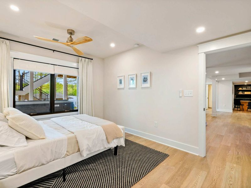 Bedroom 5 - Large window looks out to the multi-level deck and stairs, with the hallway leading to the bar area.